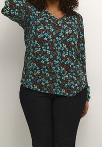 Blouse noire à manches longues avec un imprimé floral, présentant des fleurs bleues, des accents marron et un col en V. Associée à un jean foncé.