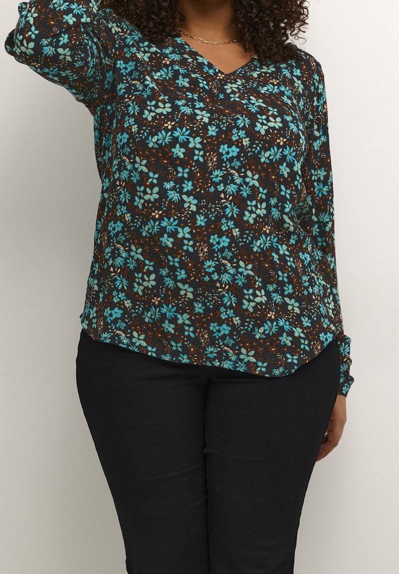 Blouse noire à manches longues avec un imprimé floral, présentant des fleurs bleues, des accents marron et un col en V. Associée à un jean foncé.