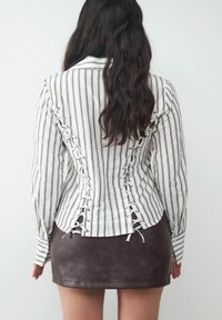 Striped blouse with lace-up detailing on the back, paired with a brown faux leather mini skirt. Long sleeves and a fitted silhouette.
