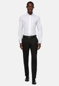 Bela srajca z dolgimi rokavi, z gumbi spredaj in na manšetah; v kombinaciji z črnimi poslovnimi hlačami in črnimi vezalkami.