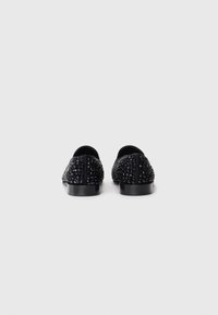 Black loafers with raised shiny black studs covering the entire surface, shown from the back on a white background.