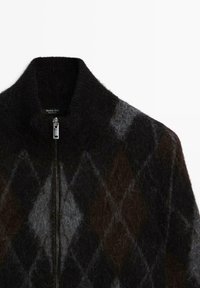 Pull zippé noir et marron duveteux avec un col montant et un motif losanges argyle en tons gris et marron.