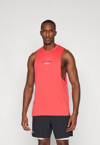 Red sleeveless athletic tank top made of soft fabric, featuring a crew neck and a logo in black, paired with dark shorts.