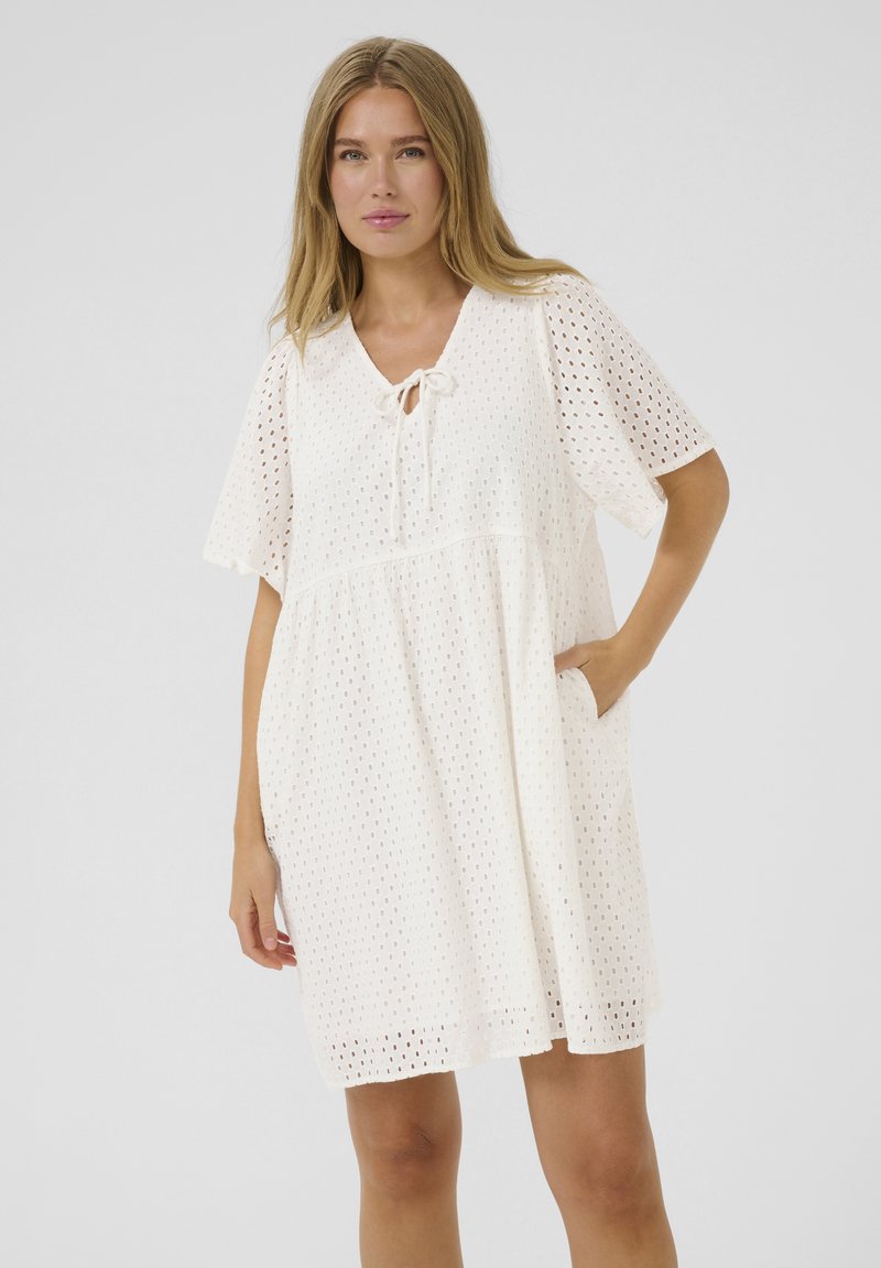 Robe blanche à manches courtes avec motif œillet, col à cordelette et poches latérales. Silhouette fluide en A avec un tissu respirant.