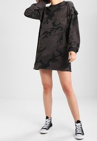 Svart kamouflage oversized sweatshirtklänning med sänkta axlar, rå kant och texturerad tyg, kombinerad med svarta högskurna sneakers.