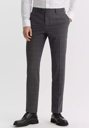 Szare kraciaste spodnie o slim fit, wykonane z teksturowanej tkaniny, z płaskim przodem i bocznymi kieszeniami, zestawione z czarnymi eleganckimi butami.
