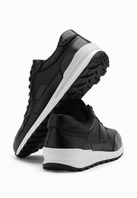 Scarpe sportive nere in pelle sintetica con tomaia texturizzata, suola bianca e suola in gomma nera con motivo. Presentano allacciatura e colletto imbottito.