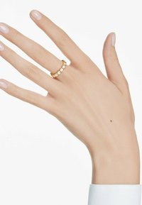 Bague en or ornée de cinq pierres précieuses transparentes disposées en motif circulaire, présentée sur une main à la peau claire et avec un vernis à ongles neutre.