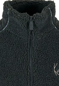 Black fleece jacket with a high collar and zip closure, featuring a soft, textured surface and a small logo accent on the front.