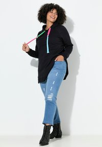 Musta huppari, jossa värikkäät nyörit, yhdistetty vaaleansinisiin kuluneisiin farkkuihin ja mustiin nilkkureihin, joissa on hopeiset niitit.