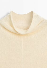 Cream-colored knitted sweater with a loose, folded turtleneck collar and visible knit texture on a white background.