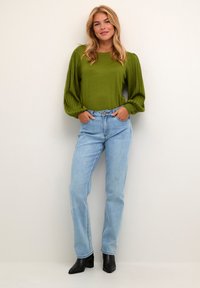 Suéter verde de punto con mangas abullonadas, combinado con jeans rectos de color azul claro. La modelo lleva botas de tacón negras hasta el tobillo. Fondo liso.