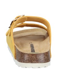 Gele suède sandaal met een gevormd kurken voetbed en een witte rubberen buitenzool. Voorzien van verstelbare banden en een plat ontwerp.
