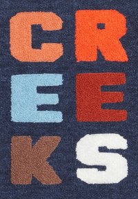 El fondo textil azul marino presenta letras en relieve en naranja, azul claro, rojo, marrón y blanco formando la palabra "CREEKS."