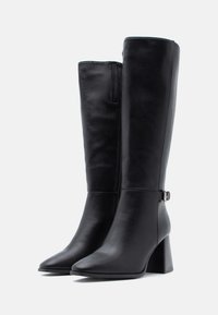 Stivali neri in pelle al ginocchio con punta affusolata, tacco spesso, zip laterale e dettaglio decorativo a fibbia sulla caviglia. Texture liscia.
