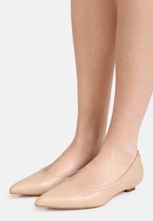 Nude pointed-toe leather ballet flats worn on bare feet, shown against a plain light background.