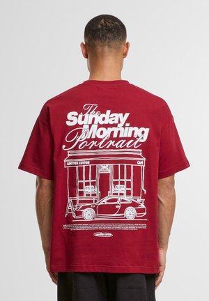 Burgundy cotton t-shirt with white graphic design featuring a café and a sports car. Short sleeves and relaxed fit.