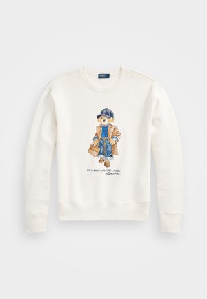 Biała bluza z nadrukiem niedźwiedzia w czapce z daszkiem, beżowym płaszczu, niebieskim swetrze, dżinsach i trzymającego brązową teczkę.