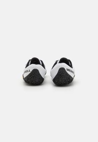 Baskets de sport blanches et noires avec une semelle extérieure texturée, arborant un design bas et le logo "MERRELL" au niveau du talon.