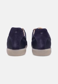 Marineblaue Sneakers mit glatten und Wildleder-Oberflächen, runden Absätzen und einer leichten Gummisohle; das Rückendesign enthält ein kleines Logo-Element.