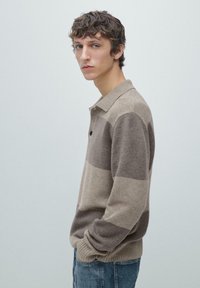 Béžový a hnědý pruhovaný svetr s polokošilovým límečkem, doplněný knoflíkovou légou a žebrovanými manžetami, ladící s džínami světlé barvy.