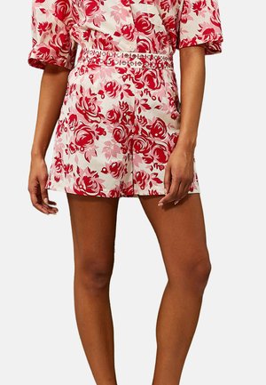Pantalones cortos con estampado floral en blanco, rosa y rojo, con un diseño ajustado y un cinturón decorativo. De longitud corta y textura suave.
