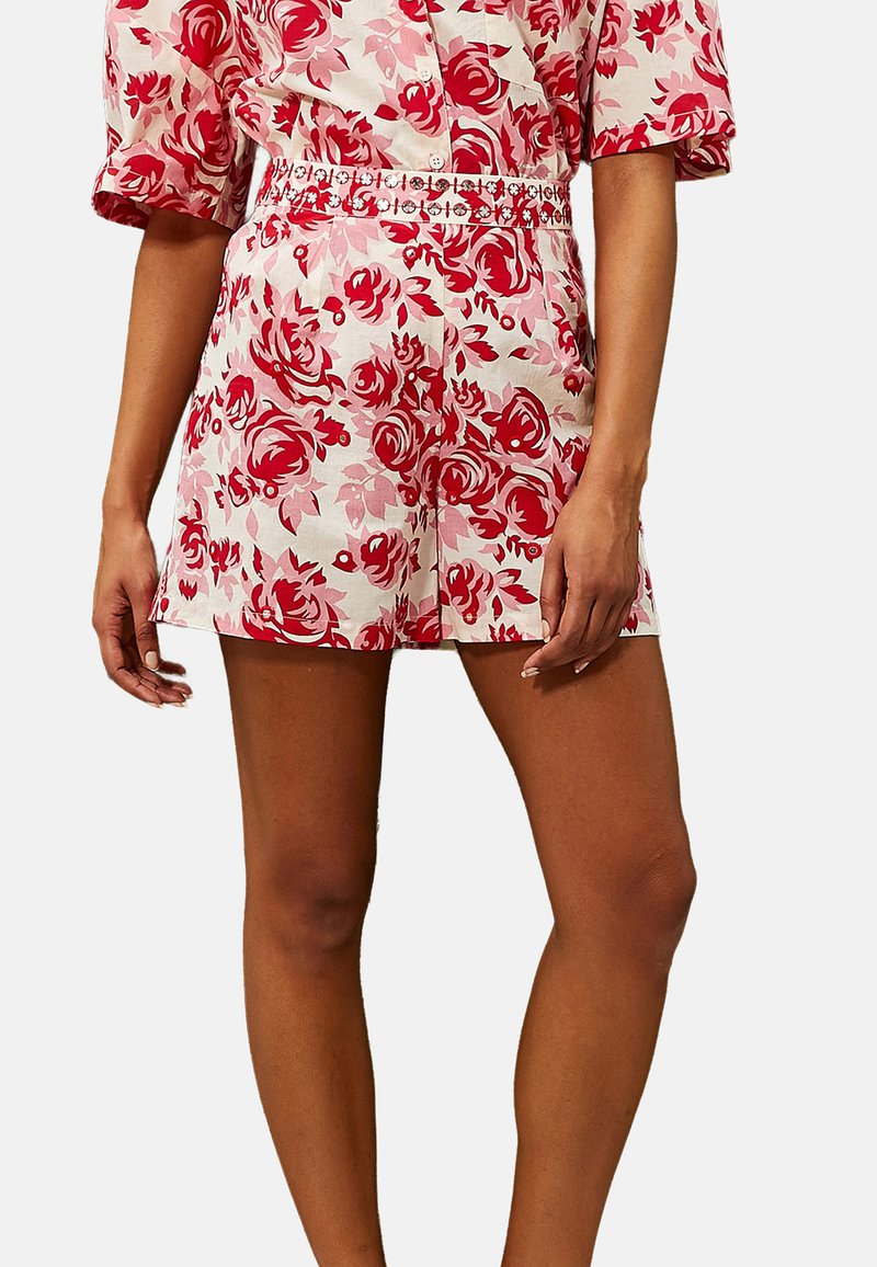 Shorts con motivo floreale in bianco, rosa e rosso, con un design aderente e una cintura decorativa. Lunghezza corta e texture liscia.