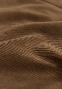 Tissu en velours côtelé marron avec une texture côtelée visible et des plis doux créant des ombres délicates.