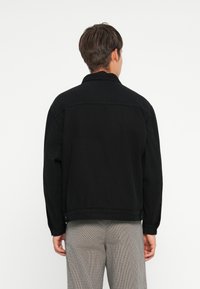 Giubbotto di jeans nero con maniche lunghe, colletto e tasche laterali. Presenta una vestibilità dritta e dettagli cuciti sulle cuciture.