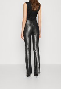 Zwarte mouwloze top gecombineerd met strakke, glanzende zilveren flared broek, die een soepele textuur en een hoge taille ontwerp laat zien.