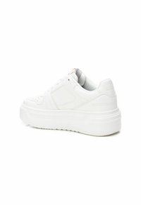 Zapatilla blanca con un exterior de cuero suave, suela gruesa, puntera redondeada y un diseño minimalista. Presenta costuras sutiles y una etiqueta de acento.