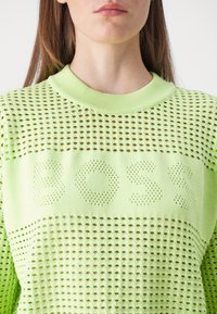 Maglione lavorato a maglia verde lime con texture perforata e colletto a coste. Presenta la scritta "BOSS" in uno stile perforato simile sul petto.