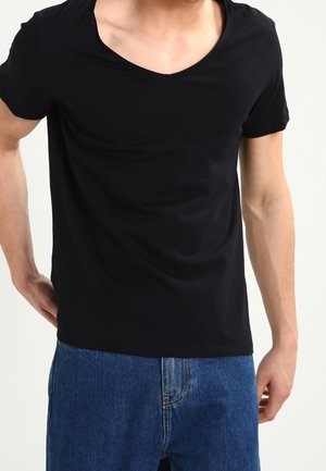 Schwarzes T-Shirt mit kurzen Ärmeln und weitem V-Ausschnitt, aus weichem Stoff, tailliert an den Schultern, kombiniert mit blauen Jeans.