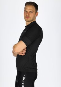 Schwarzes, kurzärmliges Radtrikot mit schlanker Passform, strukturiertem Stoff und vollem Reißverschluss. Verfügt über eine Rückentasche zur Aufbewahrung.