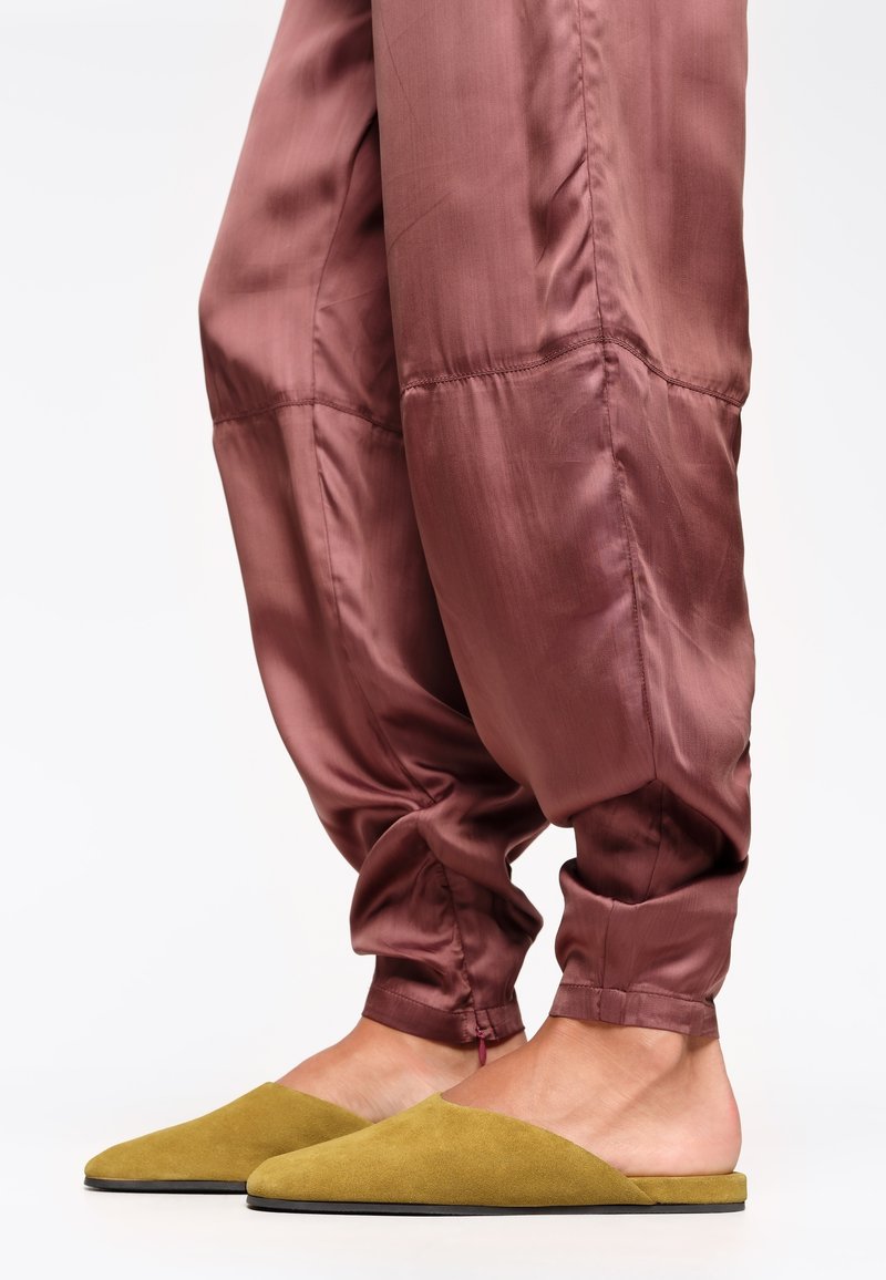 Zapatos amarillos de ante, tipo slip-on, con punta afilada y parte trasera abierta, combinados con pantalones satinados sueltos de color rosa brillante.