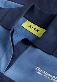 Jūras spēku un gaiši zils svītrains polo krekls ar ribotu apkakli, trim pogām un dzeltenu birku ar uzrakstu "JJXX". Iekļauj izšūtus tekstus.