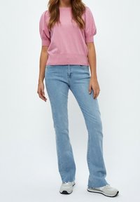 Ljusrosa stickad tröja med puffärmar och ribbad nederkant, ihop matchad med ljusblå utsvängda jeans och grå sneakers med svarta sulor.