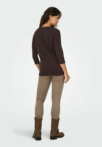 Maglia marrone a maniche lunghe, dalla forma aderente, abbinata a pantaloni skinny beige e stivaletti marroni, con dettagli in metallo argentato.