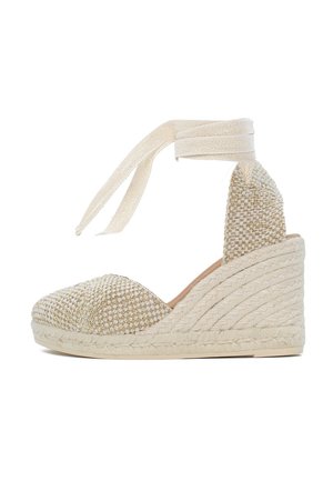 Beżowe plecione espadryle na koturnie z teksturową cholewką, okrągłym noskiem i wstążkowym zapięciem wokół kostki. Posiada naturalny obcas owinięty w jutę.