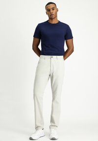 Camiseta ajustada de color azul marino combinada con pantalones gris claro, con cierre de botón. Zapatillas blancas con detalles en gris completan el atuendo.