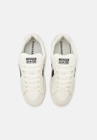 White leather sneakers with black star accents, perforated toe box, flat laces, and branded tongues. Classic low-profile design.