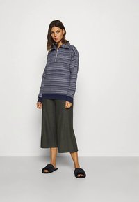 Pulover bleumarin din fleece cu model, prevăzut cu fermoar scurt, asortat cu culotte gri largi și papuci închiși la culoare, având manșete și tiv striate.