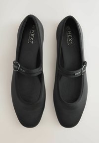 Ballerines noires avec un bout arrondi, sangle élastique et petite boucle métallique en accent. Fini mat lisse et doublure en tissu doux.
