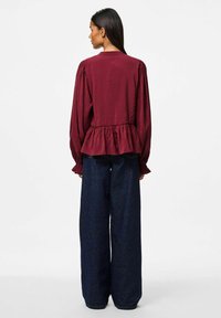 Burgundy långärmad peplumblus med rund krage, samlade axlar och volangärmar, kombinerad med vida mörk denimjeans.