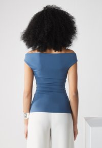 Top azul sin hombros con textura fruncida en la cintura, combinado con pantalones blancos de pierna ancha. Tejido suave y diseño ajustado.