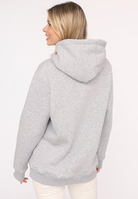 Sudadera gris claro hecha de una tela suave, con un bolsillo canguro, puños de canalé y una capucha con cordón. La vista trasera muestra un corte relajado.