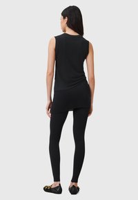 Top senza maniche nero abbinato a leggings neri e scarpe basse. Il top ha una vestibilità comoda e un orlo curvo; il tessuto appare morbido ed elastico.