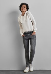 Haut à capuche blanc avec cordons de serrage, associé à un jean skinny gris. Baskets blanches avec des semelles claires. Design simple et coupe moderne.