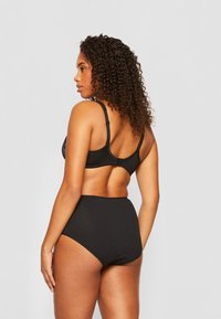 Zwarte beha met verstelbare bandjes en haaksluiting, gecombineerd met hoge zwarte panties. Glad stof, minimalistisch ontwerp, geen patronen.