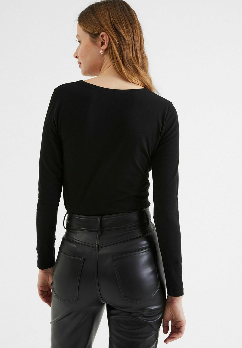 Czarny longsleeve z dekoltem typu scoop, w zestawieniu z wysokim stanem czarnych skórzanych spodni z widocznymi kieszeniami i smukłym, dopasowanym krojem.